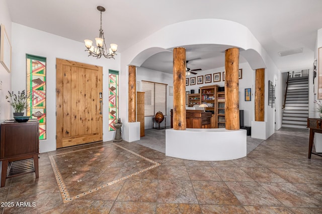 entrance foyer with ceiling fan with notable chandelier, arched walkways, stone finish floor, visible vents, and stairs