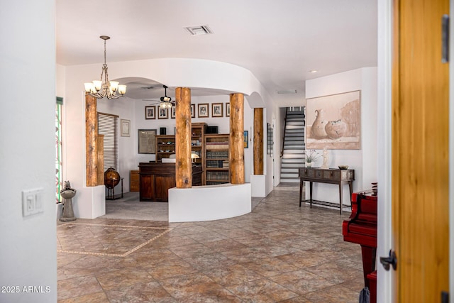 foyer with ceiling fan with notable chandelier, arched walkways, stone finish floor, visible vents, and stairs