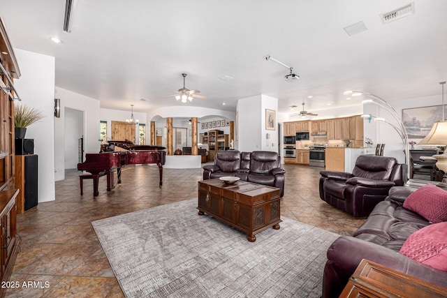 living area with visible vents, a ceiling fan, arched walkways, and stone finish flooring