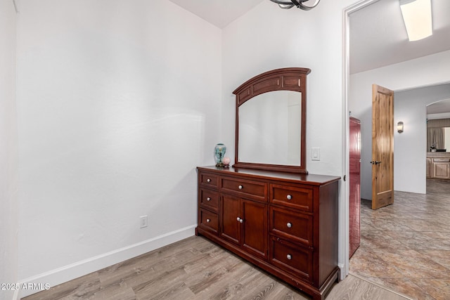 hallway with baseboards, arched walkways, and light wood-style floors