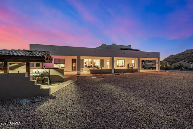 back of house at dusk featuring a patio area and stucco siding