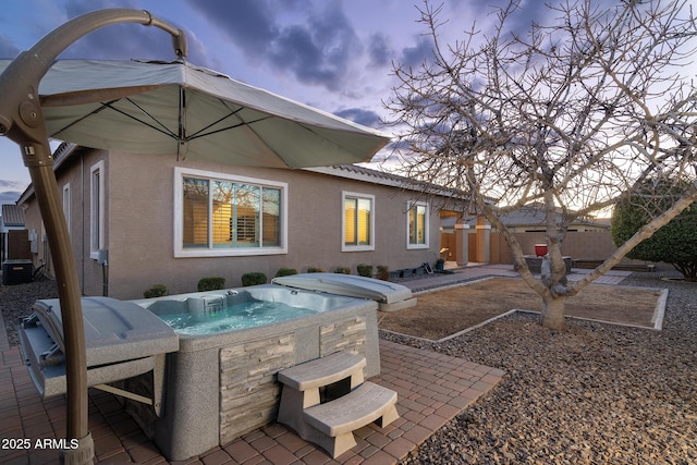 back house at dusk featuring a hot tub and a patio