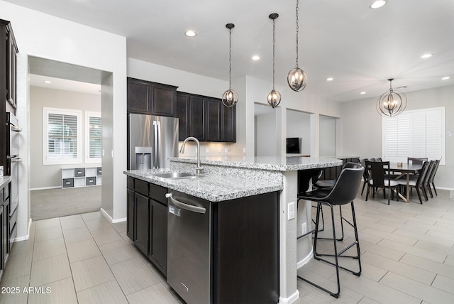 kitchen with appliances with stainless steel finishes, sink, hanging light fixtures, a kitchen island with sink, and light stone countertops