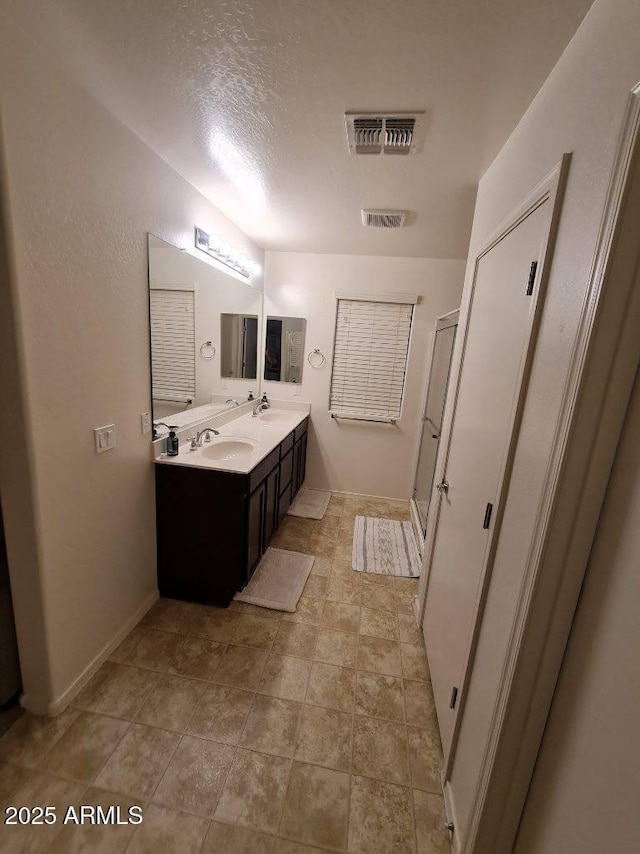 bathroom with a sink, visible vents, double vanity, and a shower stall