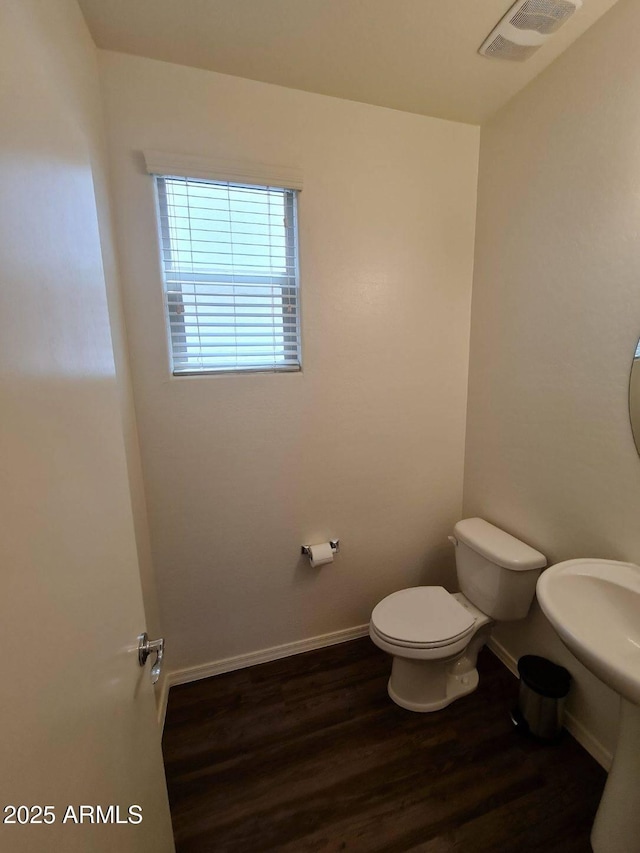 half bath featuring toilet, wood finished floors, visible vents, and baseboards