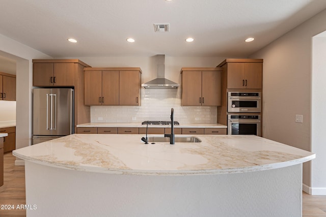 kitchen featuring an island with sink, stainless steel appliances, and wall chimney range hood