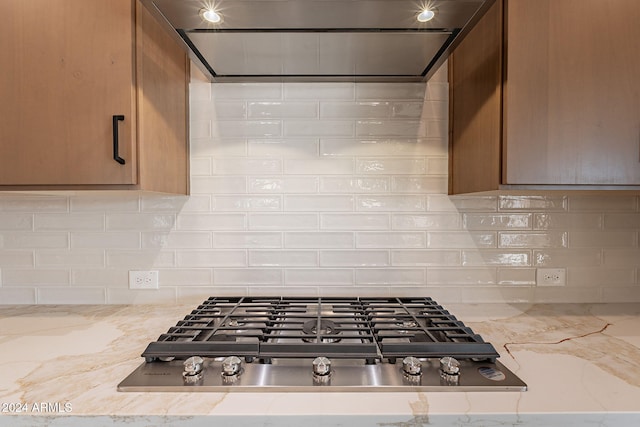 kitchen featuring wall chimney exhaust hood, light stone counters, backsplash, and stainless steel gas cooktop