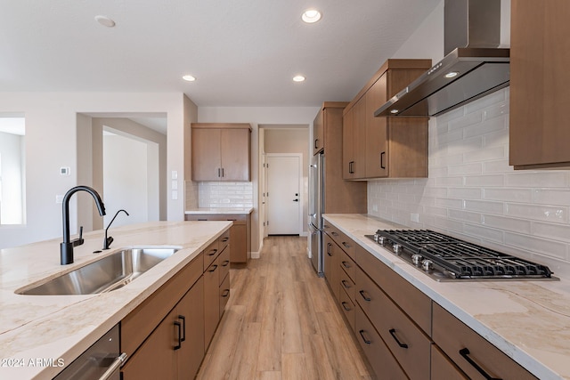 kitchen with backsplash, stainless steel appliances, sink, wall chimney range hood, and light hardwood / wood-style flooring