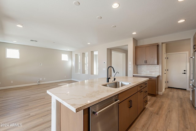 kitchen with a kitchen island with sink, sink, light hardwood / wood-style flooring, light stone countertops, and stainless steel appliances