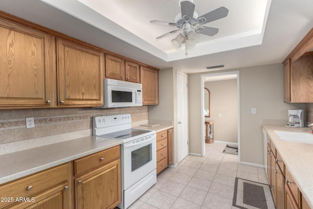 kitchen with light tile patterned flooring, sink, tasteful backsplash, a raised ceiling, and white appliances