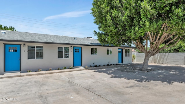 ranch-style house with fence, a shingled roof, and stucco siding