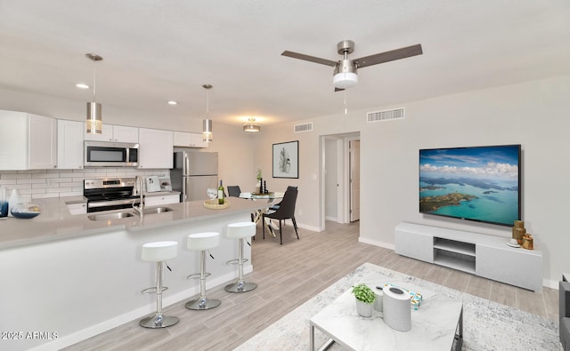 living area featuring visible vents, baseboards, light wood-type flooring, and ceiling fan
