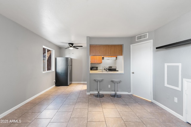 kitchen with ceiling fan, exhaust hood, kitchen peninsula, stainless steel refrigerator, and a breakfast bar area