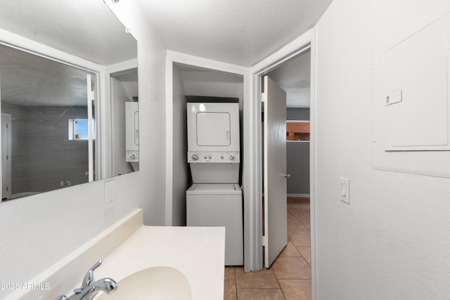 bathroom featuring stacked washer / dryer, sink, tile patterned floors, and a textured ceiling