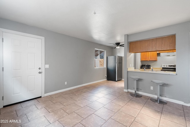 kitchen featuring light tile patterned floors, a kitchen bar, kitchen peninsula, ceiling fan, and appliances with stainless steel finishes