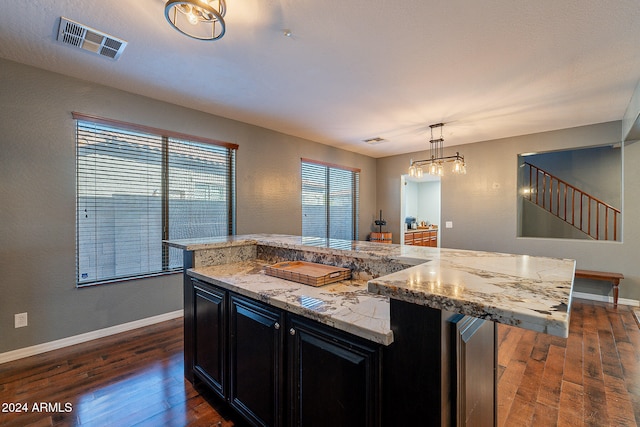 kitchen featuring hanging light fixtures, light stone countertops, dark hardwood / wood-style floors, and a spacious island