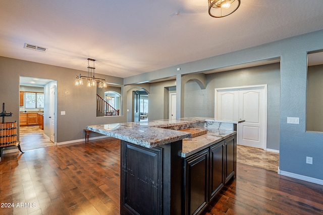 kitchen with hanging light fixtures, dark hardwood / wood-style floors, a kitchen island, and light stone countertops