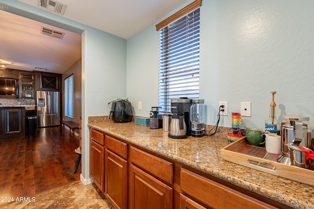 kitchen with stainless steel refrigerator with ice dispenser, hardwood / wood-style flooring, and light stone countertops