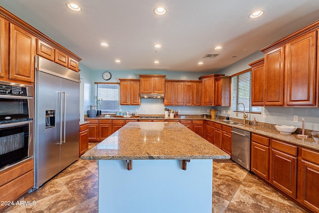 kitchen featuring stainless steel appliances, sink, light stone counters, a breakfast bar area, and a center island