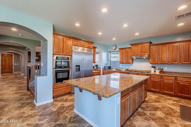 kitchen featuring a kitchen bar, appliances with stainless steel finishes, a kitchen island, and light stone countertops