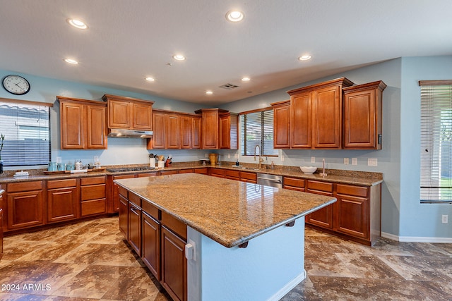 kitchen with sink, light stone counters, appliances with stainless steel finishes, and a center island