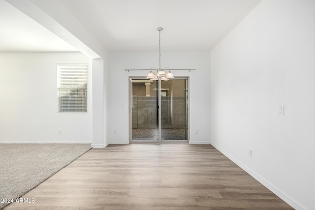 empty room featuring wood-type flooring and an inviting chandelier