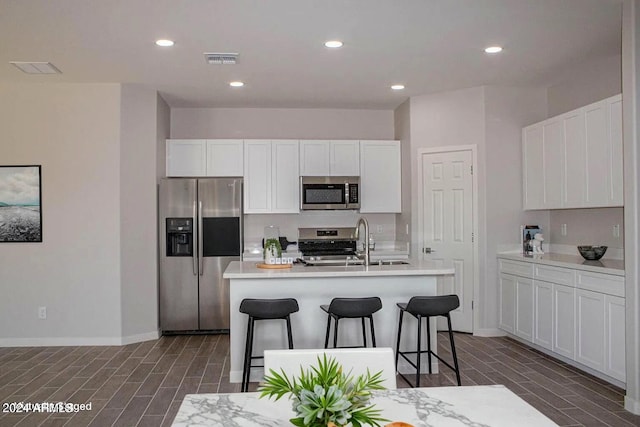 kitchen featuring stainless steel appliances, sink, white cabinets, a breakfast bar area, and an island with sink