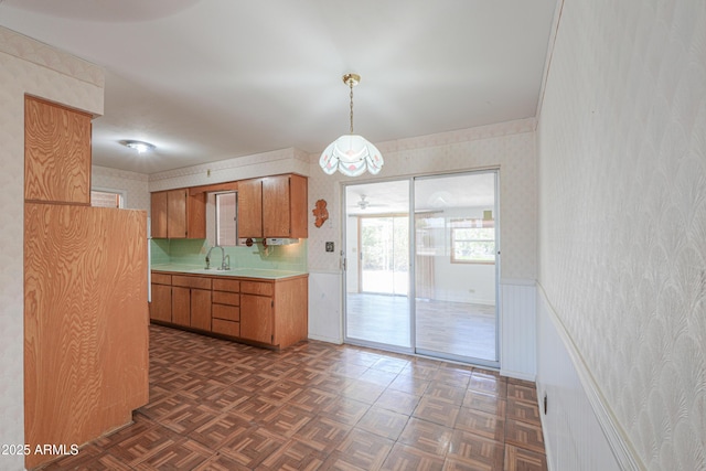 5228 E Des Moines St, Mesa, AZ 85205 - kitchen with wallpapered walls, light countertops, a sink, brown cabinetry, and pendant lighting
