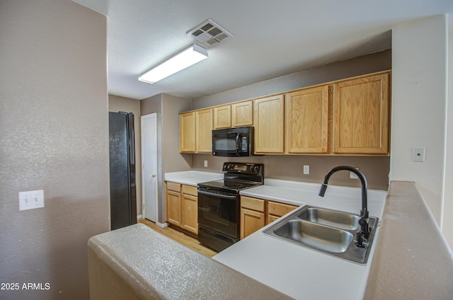 kitchen with light countertops, visible vents, light brown cabinetry, a sink, and black appliances