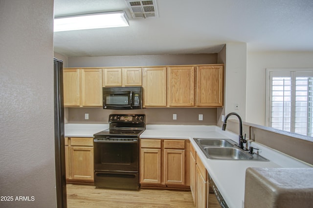 kitchen with light wood finished floors, visible vents, light countertops, black appliances, and a sink