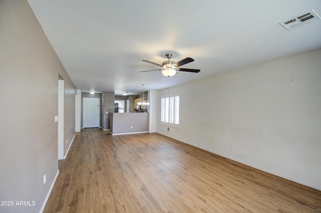 unfurnished living room featuring ceiling fan with notable chandelier, visible vents, baseboards, and wood finished floors