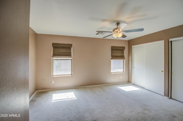 unfurnished bedroom featuring multiple closets, carpet, visible vents, and a ceiling fan