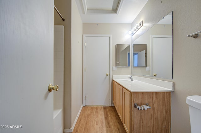 bathroom with bathtub / shower combination, a raised ceiling, toilet, vanity, and wood finished floors