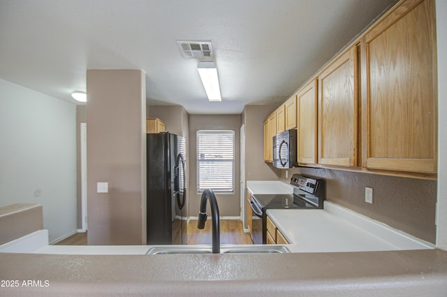 kitchen with visible vents, light countertops, black appliances, light brown cabinets, and a sink