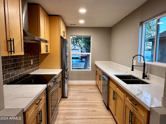 kitchen with light stone counters, sink, light hardwood / wood-style flooring, wall chimney exhaust hood, and appliances with stainless steel finishes