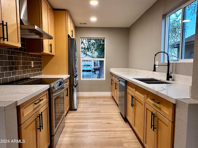 kitchen with stainless steel appliances, wall chimney exhaust hood, sink, and plenty of natural light