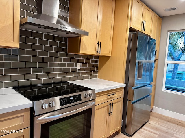 kitchen featuring tasteful backsplash, light stone countertops, stainless steel appliances, light wood-type flooring, and wall chimney range hood