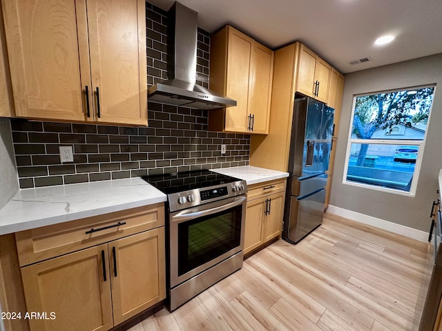 kitchen featuring light stone counters, light hardwood / wood-style floors, wall chimney exhaust hood, decorative backsplash, and appliances with stainless steel finishes