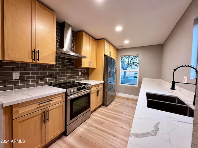 kitchen featuring sink, light hardwood / wood-style flooring, black fridge with ice dispenser, wall chimney range hood, and stainless steel stove