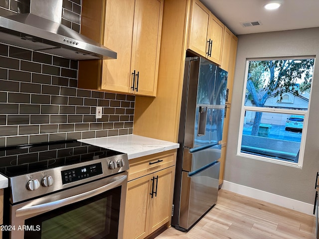 kitchen featuring light stone counters, light hardwood / wood-style floors, wall chimney exhaust hood, stainless steel appliances, and decorative backsplash