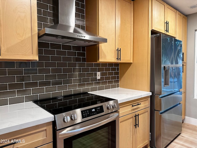 kitchen featuring decorative backsplash, refrigerator with ice dispenser, high end stove, wall chimney exhaust hood, and light hardwood / wood-style flooring