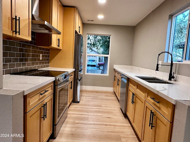 kitchen featuring light stone counters, sink, light hardwood / wood-style flooring, wall chimney range hood, and stainless steel appliances