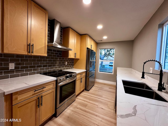 kitchen with black fridge, sink, stainless steel stove, wall chimney exhaust hood, and light hardwood / wood-style flooring