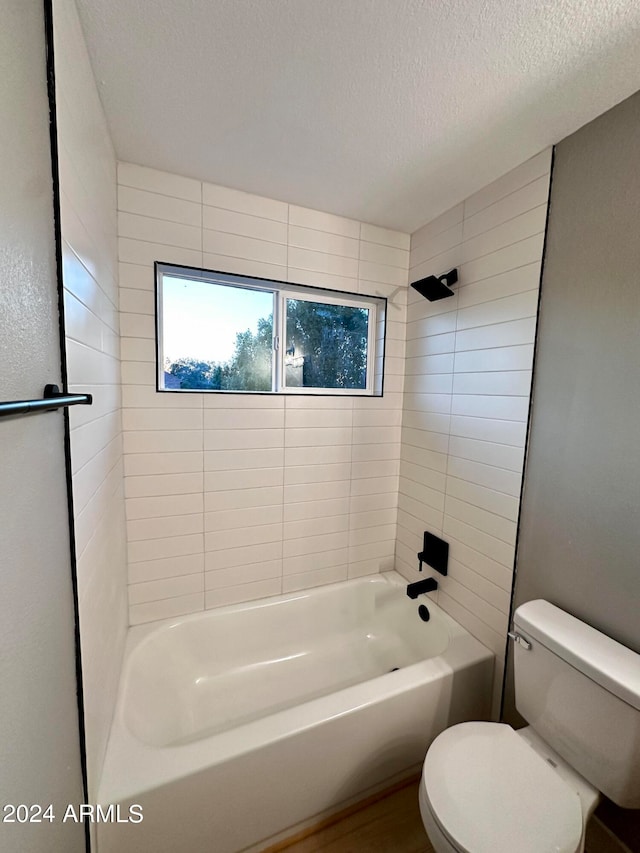 bathroom with a textured ceiling, tiled shower / bath combo, and toilet