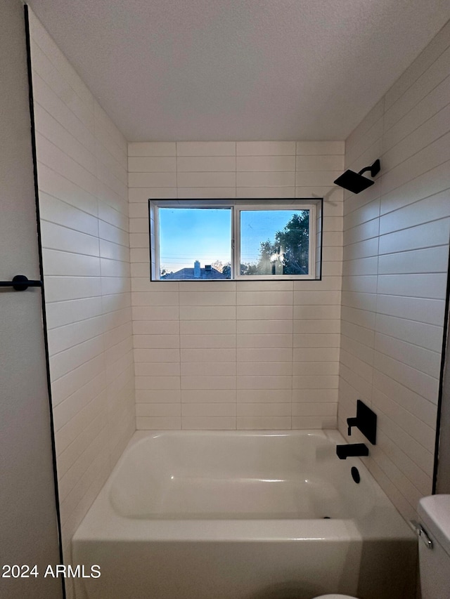 bathroom featuring a textured ceiling, toilet, and tiled shower / bath