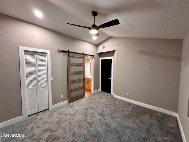 unfurnished bedroom featuring a closet, carpet flooring, lofted ceiling, a barn door, and ceiling fan