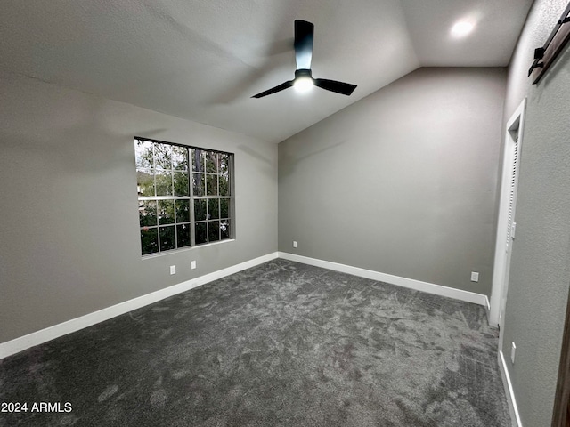 spare room featuring dark carpet, vaulted ceiling, and ceiling fan