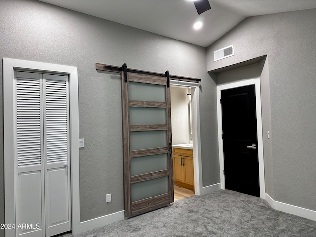 unfurnished bedroom featuring ceiling fan, lofted ceiling, carpet, a barn door, and ensuite bathroom