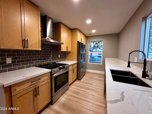 kitchen featuring light hardwood / wood-style floors, wall chimney exhaust hood, sink, black fridge, and stainless steel range