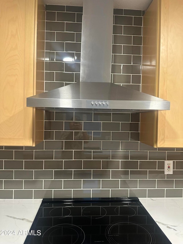 details with decorative backsplash, wall chimney exhaust hood, light stone countertops, and black stovetop